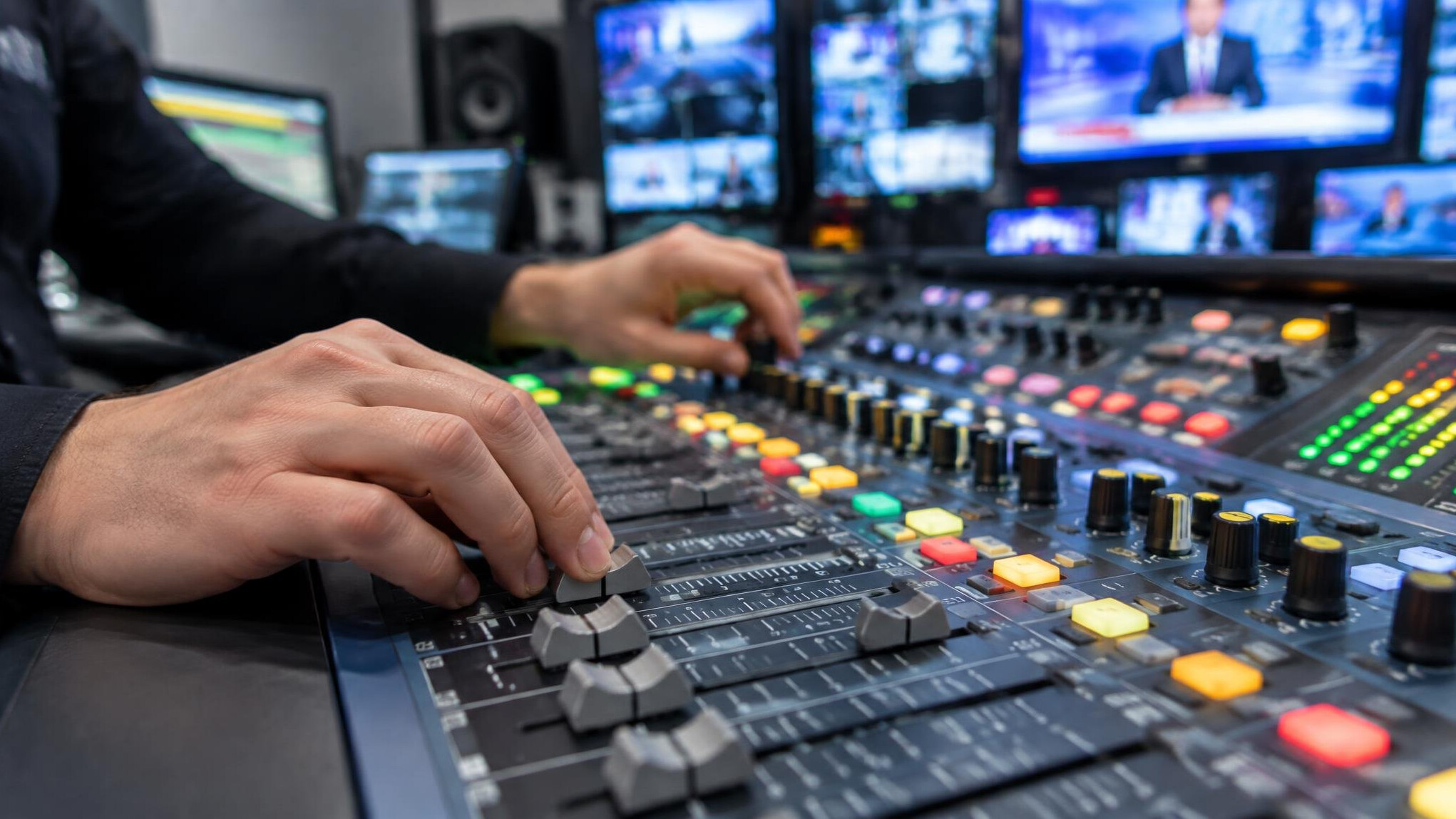 Sound engineer adjusting sliders on an audio mixing console in a broadcast control room